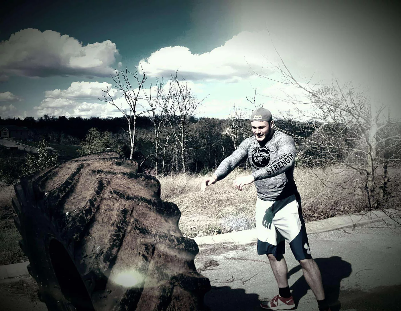 Rick Koenig flipping a tire outdoors in a Strength hoodie
